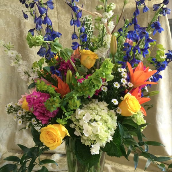 Tall mixed bouquet in a clear glass vase with blue, yellow, orange, and white flowers