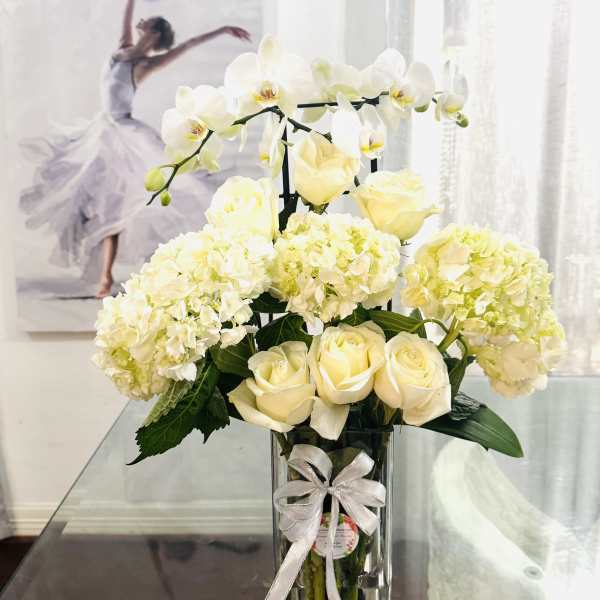White roses and hydrangeas in a clear vase with orchids and a ribbon