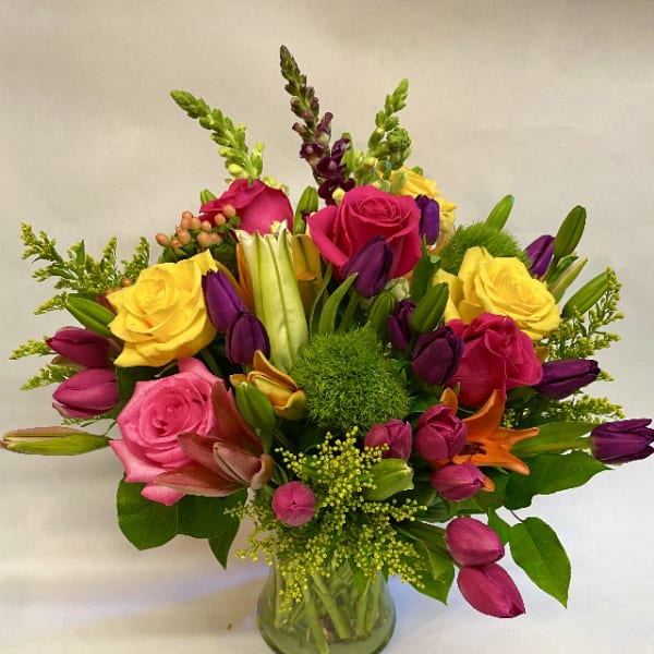 Mixed bouquet of roses, tulips, lilies, and snapdragons in a glass vase