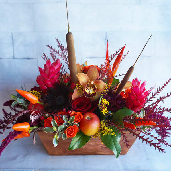 Tropical floral arrangement with red and orange blooms in a wooden container