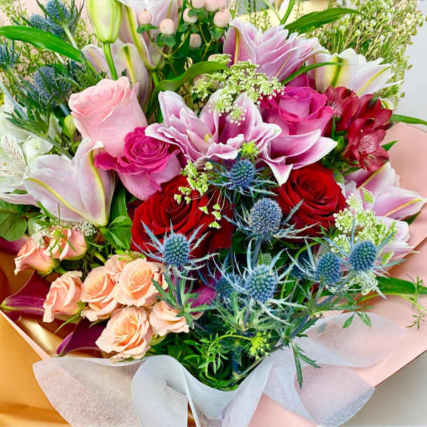 Mixed bouquet of roses, lilies, and blue thistle in pastel wrapping