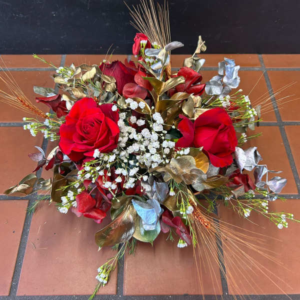 Low event centerpiece with red roses, white filler blooms, metallic foliage, and wheat accents.