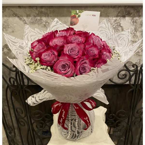 Bouquet of pink roses wrapped in white paper with a red ribbon
