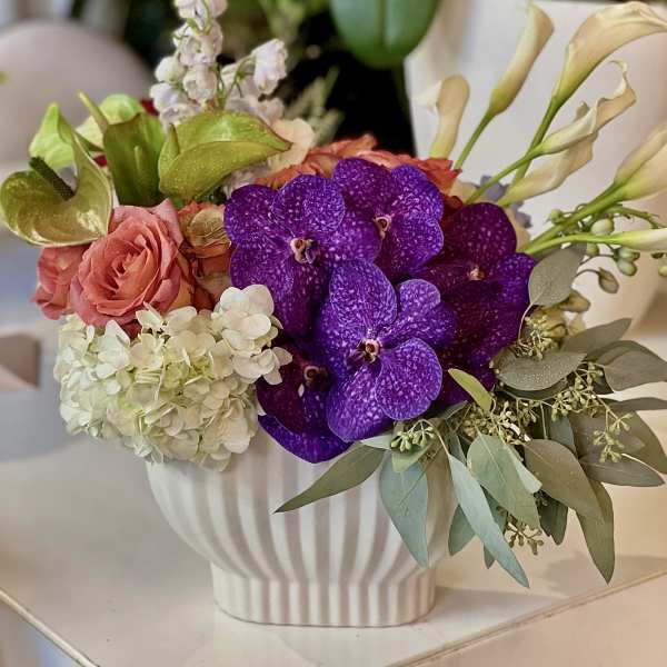 Bouquet of purple orchids, pink roses, and white hydrangea in a white vase