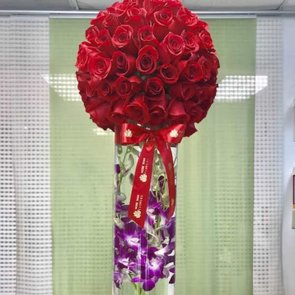 Tall glass vase with submerged purple orchids topped by a large red rose sphere and red ribbon