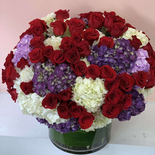 Large bouquet of red roses, white hydrangeas, and purple hydrangeas in a glass vase