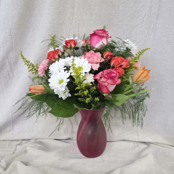 Mixed bouquet of pink roses, white daisies, and orange tulips in a frosted pink vase