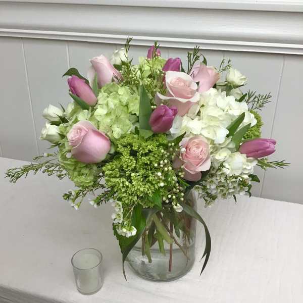 Pink roses and tulips with white hydrangeas in a clear glass vase on a table