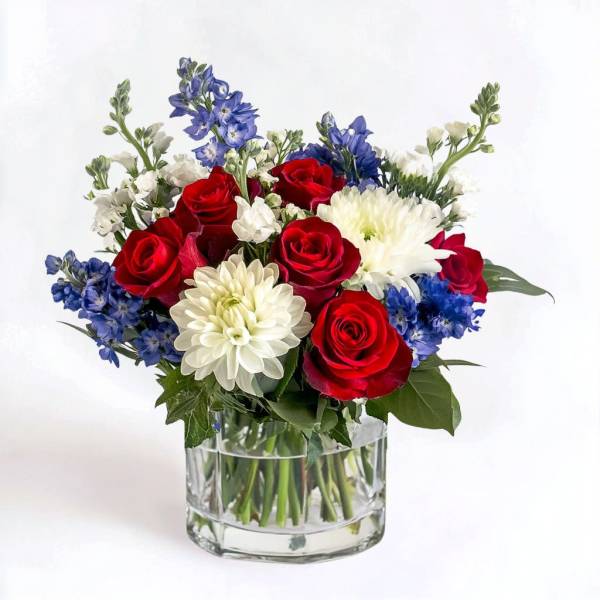 Red roses, white chrysanthemums, and blue flowers in a clear glass vase