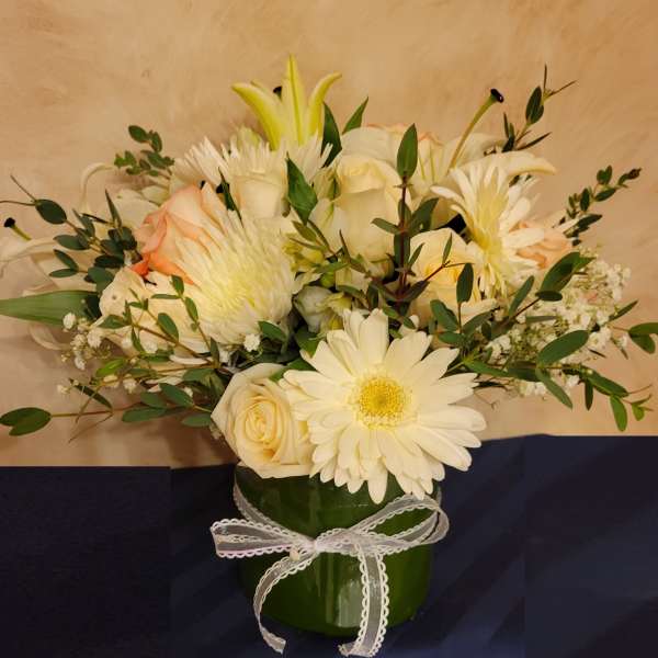 Cream and white bouquet in a green vase with a white ribbon