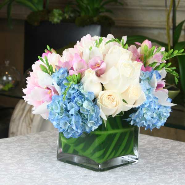 Pink and white bouquet with blue hydrangeas in a square glass vase