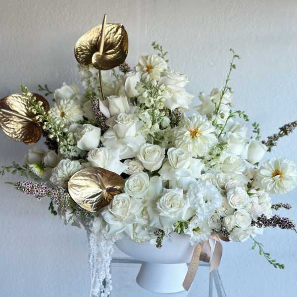 White rose bouquet in a white vase with gold anthurium leaves