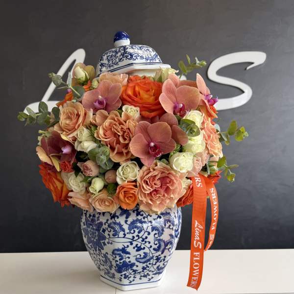 Bouquet of peach and orange roses with orchids in a blue-and-white vase