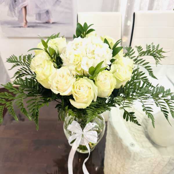 White roses and hydrangeas in a glass vase with a white ribbon