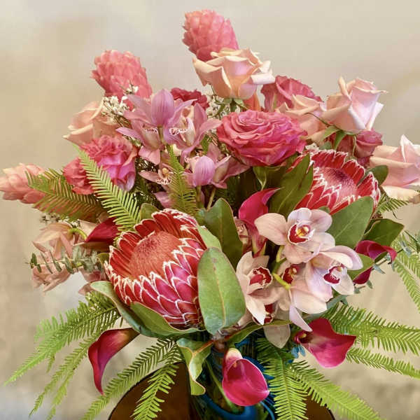 Pink and red tropical bouquet with roses, orchids, and protea in a vase