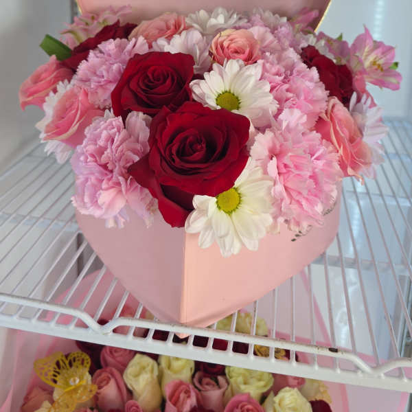 Pink heart-shaped box filled with red and pink roses and daisies