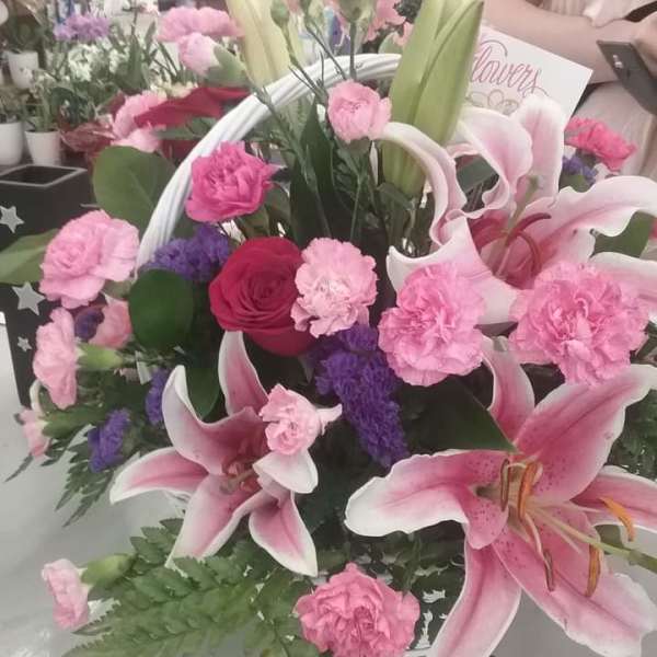 Basket arrangement of pink lilies, pink carnations, purple filler, and a red rose