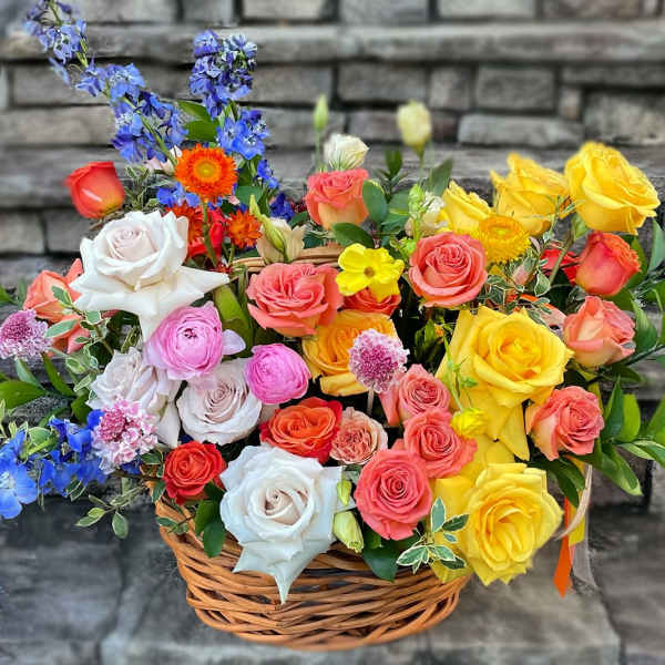 Colorful mixed basket of roses and other blooms in pink, yellow, orange, and blue.