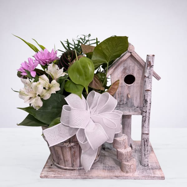 Pink and white flowers arranged with greenery in a rustic birdhouse planter