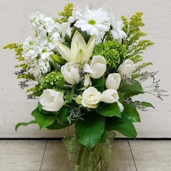 White floral arrangement in a clear glass vase with green accents