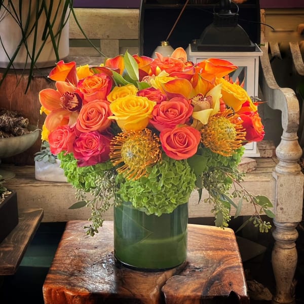 Bright bouquet of orange, yellow, and pink flowers in a green vase
