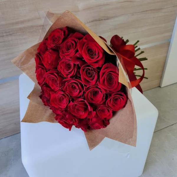 Large bouquet of red roses wrapped in brown paper and tied with a red ribbon