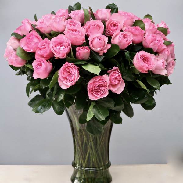 Tall bouquet of pink roses densely arranged in a clear glass vase