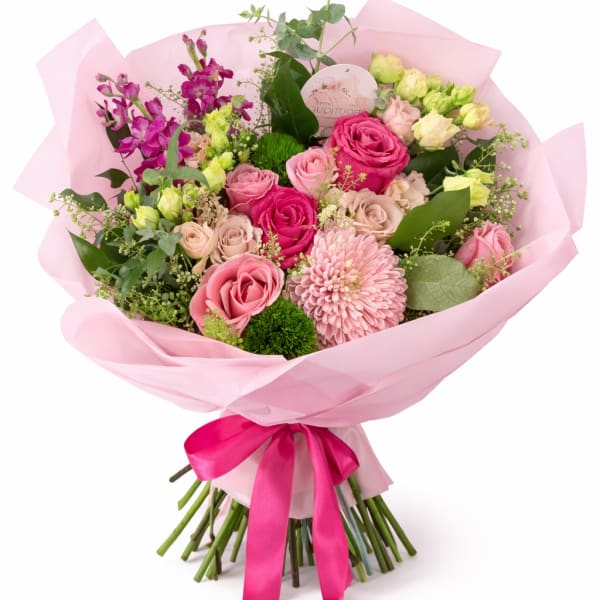 Hand-tied bouquet of pink roses, mums, and mixed blooms wrapped in pink paper with a satin bow.