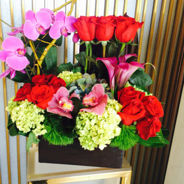 Arrangement of red roses, pink orchids, and calla lilies in a dark box
