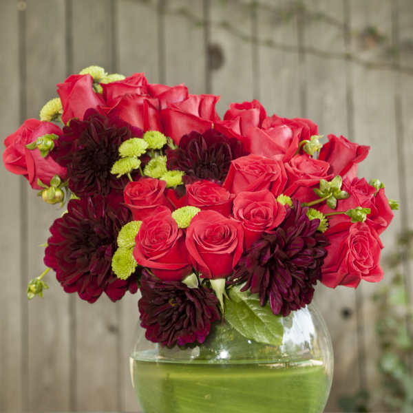 Red roses and dark burgundy blooms in a round glass vase