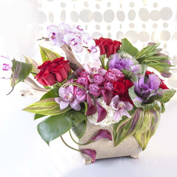 Mixed bouquet with red roses, pink orchids, and purple flowers in a woven vase