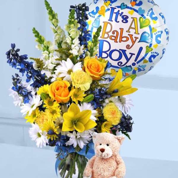 Yellow and white flower arrangement with blue accents in a vase, with baby boy balloon and teddy bear.