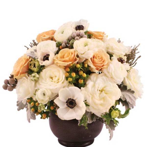 Low arrangement of white ranunculus and anemones with peach roses in a dark round bowl vase