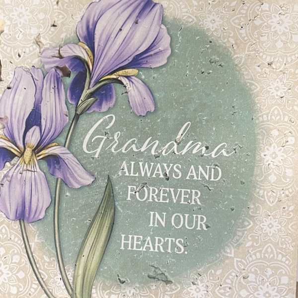 Purple flowers on a memorial plaque reading "Grandma always and forever in our hearts."