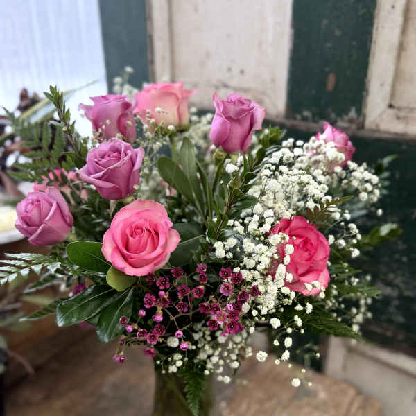 Pink and lavender roses arranged in a glass vase with white baby's breath