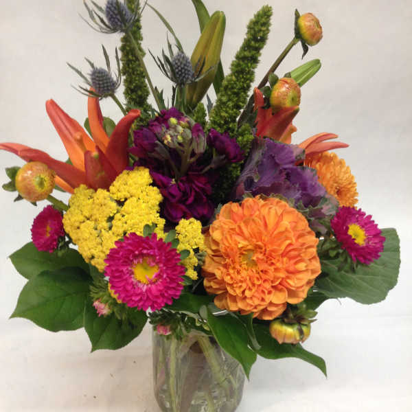 Bright mixed arrangement of orange, yellow, and pink flowers in a clear glass vase