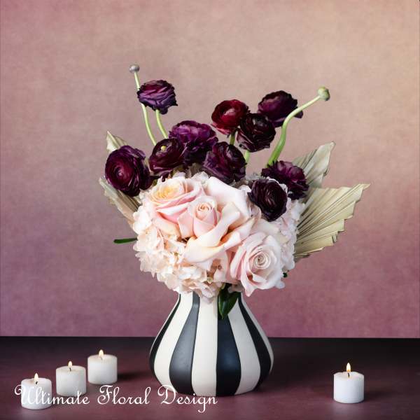Pink and burgundy roses in a striped vase with candles nearby