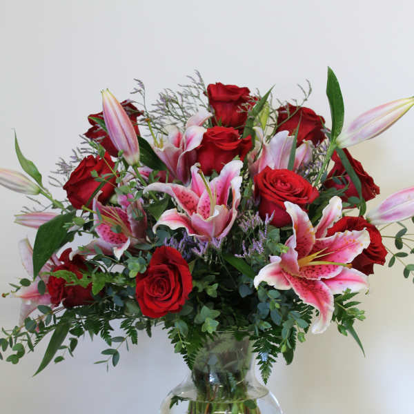 Tall arrangement of red roses and pink lilies in a clear glass vase