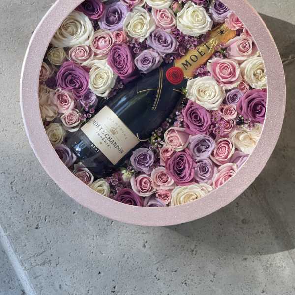 Round pink box filled with roses and a champagne bottle