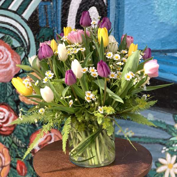 Mixed tulips and small white daisies in a clear glass vase
