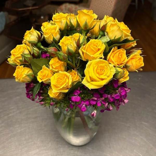 Yellow roses and small purple flowers arranged in a clear glass vase