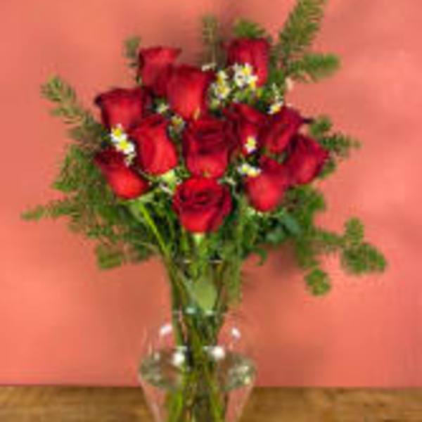 Red roses arranged in a clear glass vase with greenery
