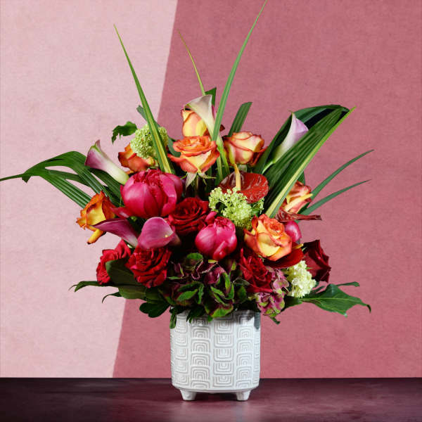 Mixed bouquet of red, pink, and orange flowers in a white patterned vase