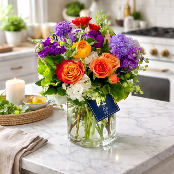 Colorful bouquet of roses and purple blooms in a glass vase