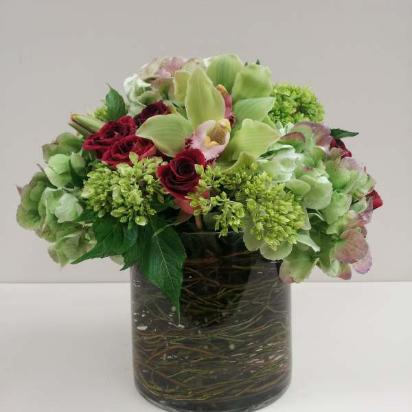 Mixed green and burgundy flowers arranged in a glass vase