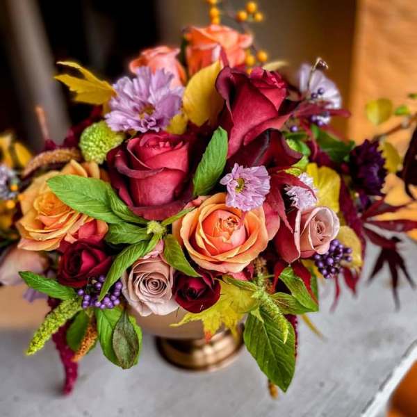 Bouquet of roses, calla lilies, and small purple flowers in a gold vase