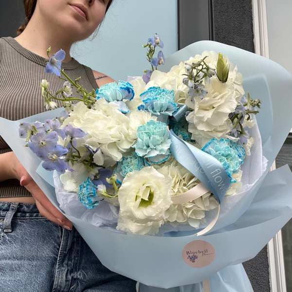 Bouquet of white hydrangeas and blue carnations wrapped in pale blue paper