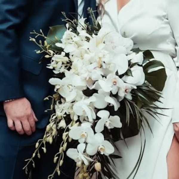 Cascading bridal bouquet of white orchids held by a bride in a white dress