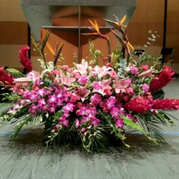 Large pink and red tropical altar spray with lilies and orchids arranged low and wide on a stage