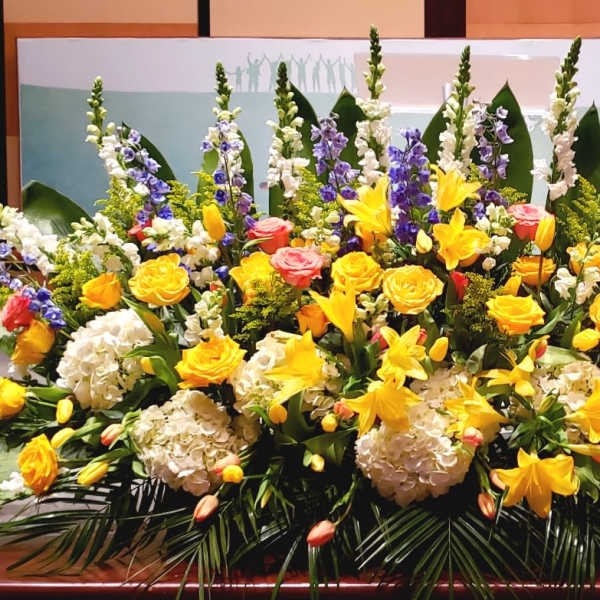 Large altar flower arrangement with yellow lilies and roses, white hydrangeas, pink roses, and blue delphinium.